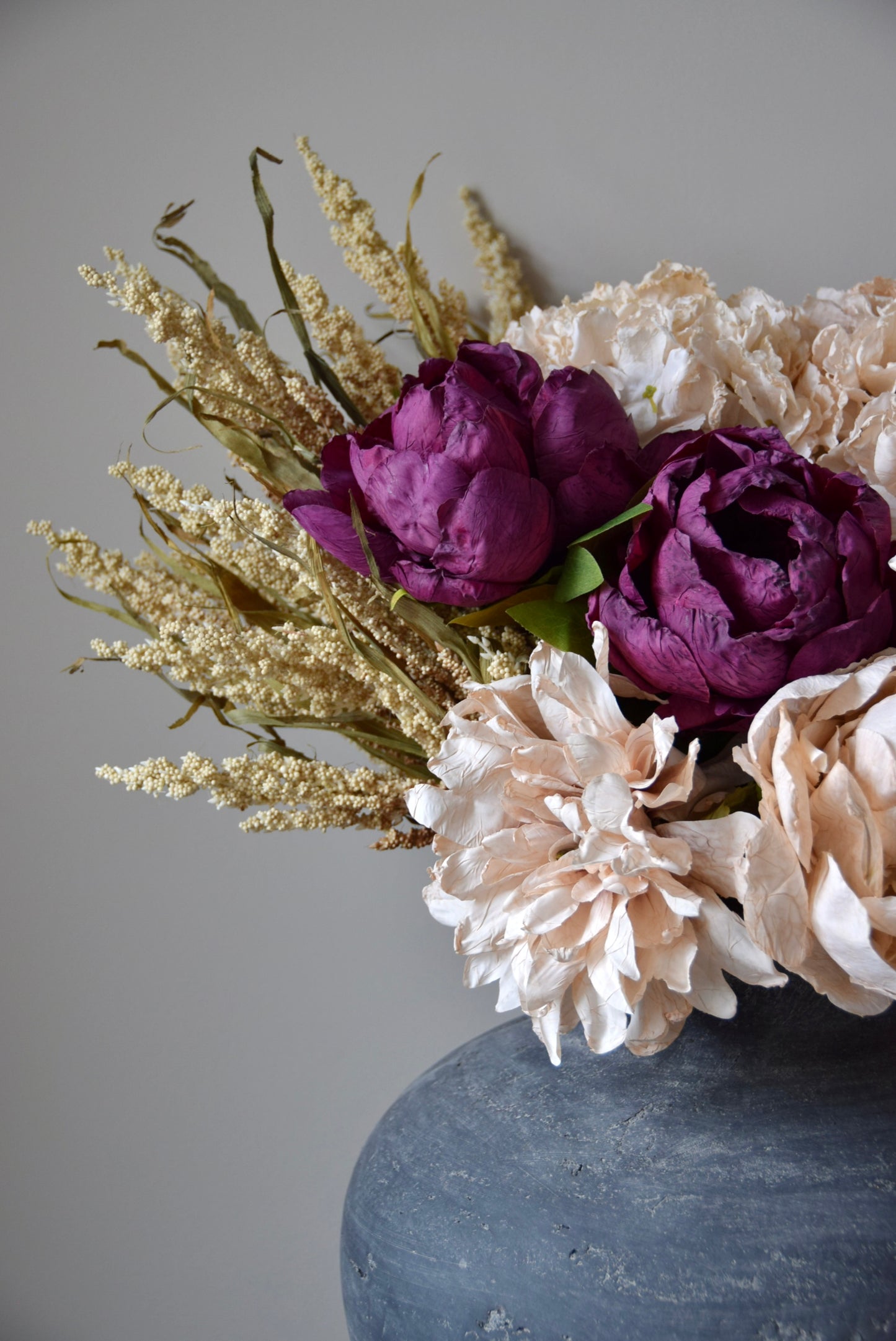 Floral arrangement with purple and beige flowers in a dark vase against a gray background