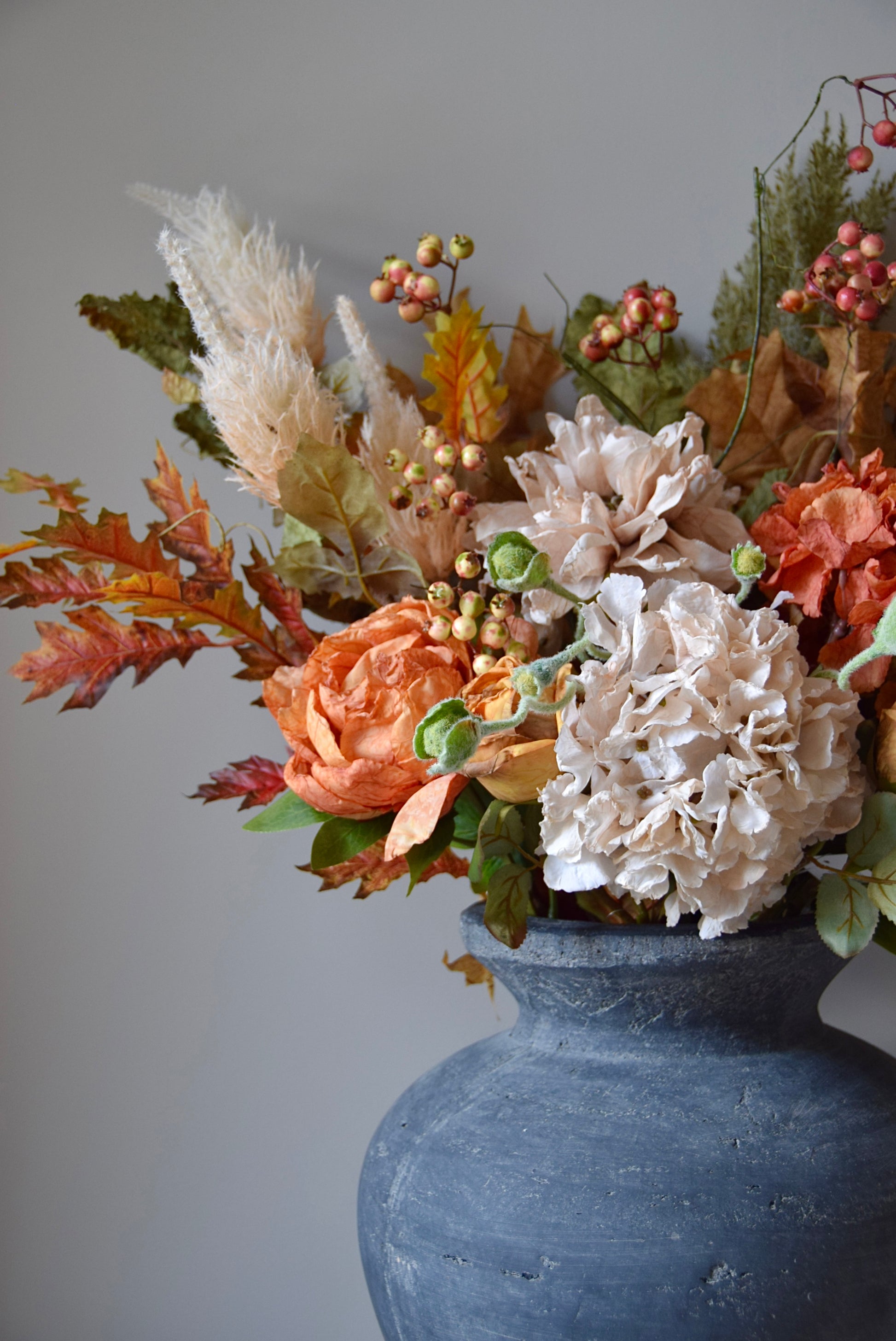 Autumnal floral arrangement in a grey vase against a grey background