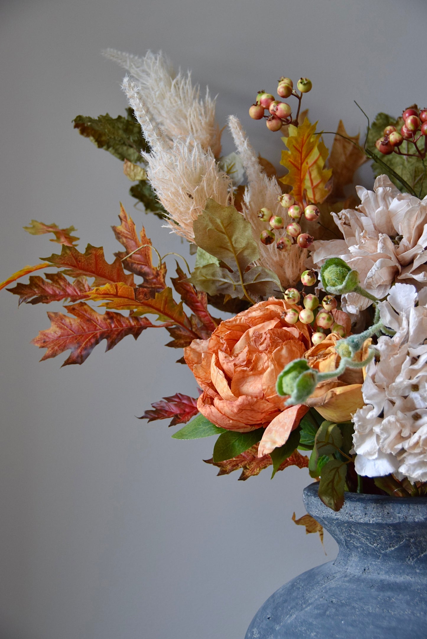 Decorative floral arrangement with autumn leaves in a grey vase against a grey background
