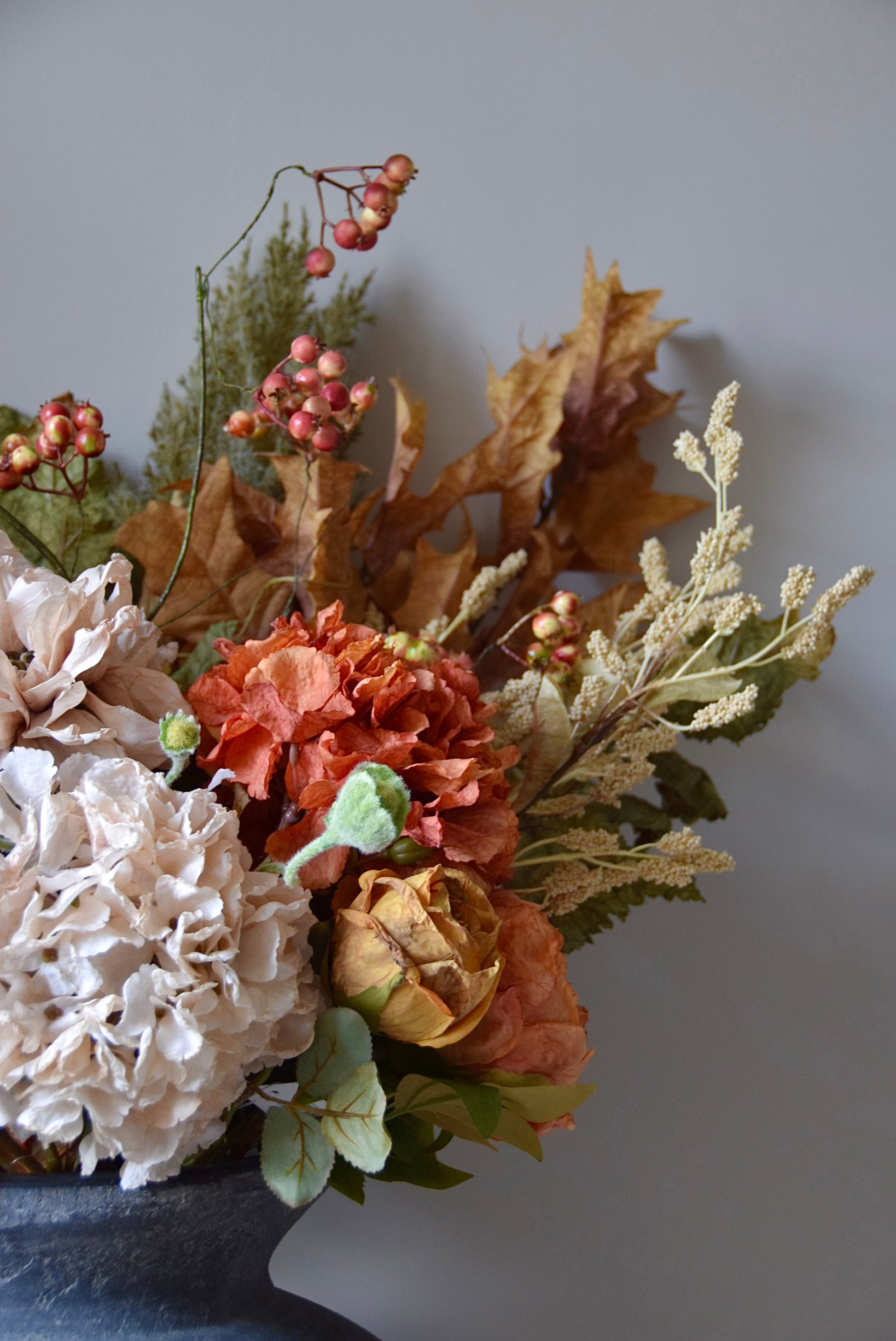 Autumnal floral arrangement with hydrangeas, berries, and leaves on a grey background