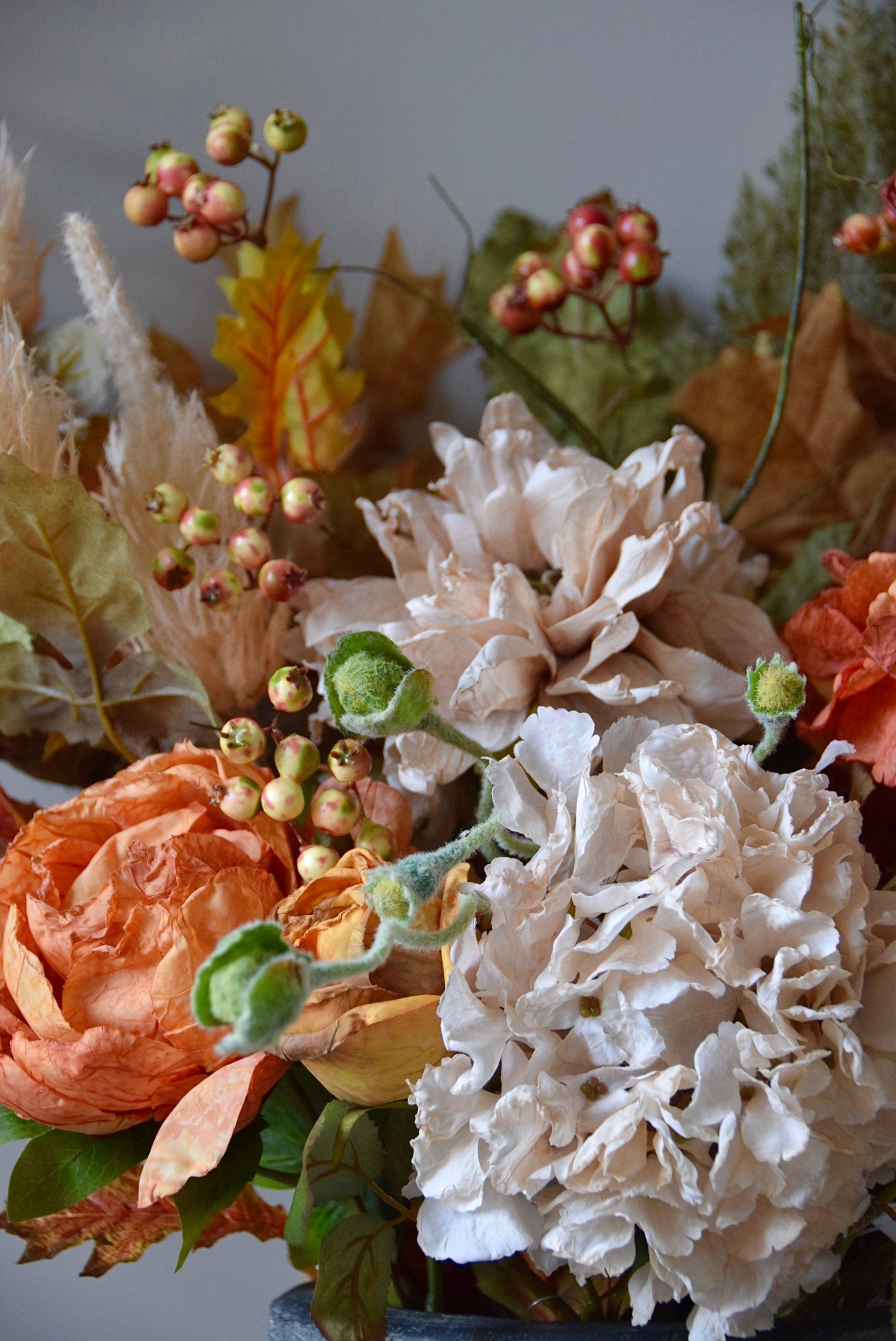Close-up of a floral arrangement with white, orange, and green flowers on a grey background