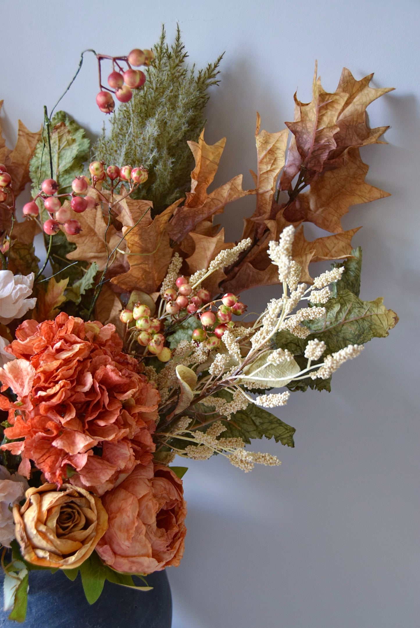 Autumn-themed floral arrangement with leaves and berries on a plain background