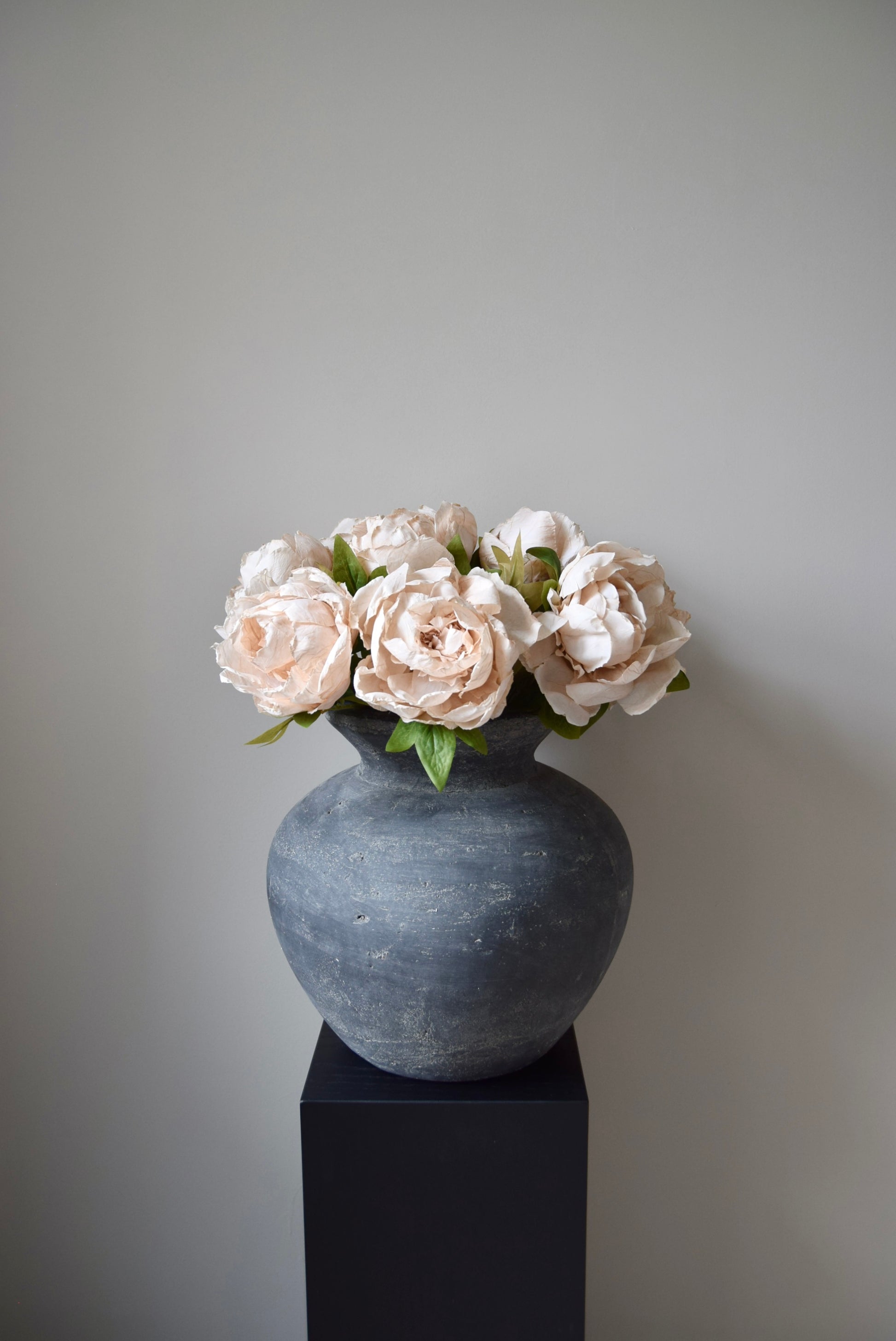 Grey vase with cream flowers on a black pedestal against a grey background
