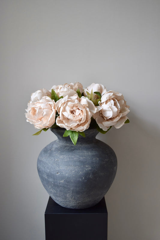 Grey vase with cream flowers on a black stand against a grey background