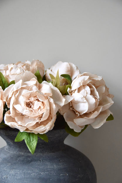 Beige flowers in a dark grey vase against a plain background