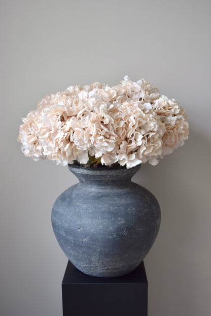 Grey vase with cream flowers against a plain background