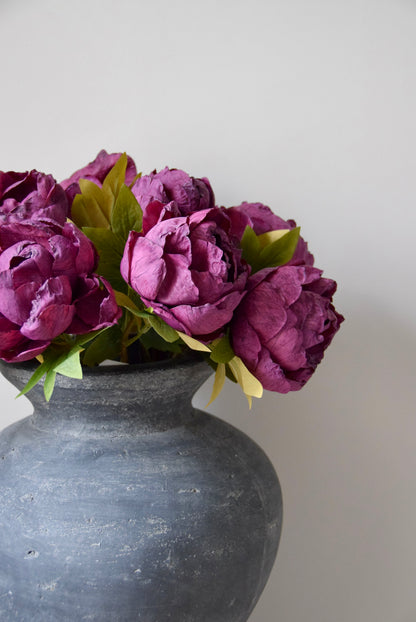 Bunch of burgundy peonies in a grey vase on a plain background.