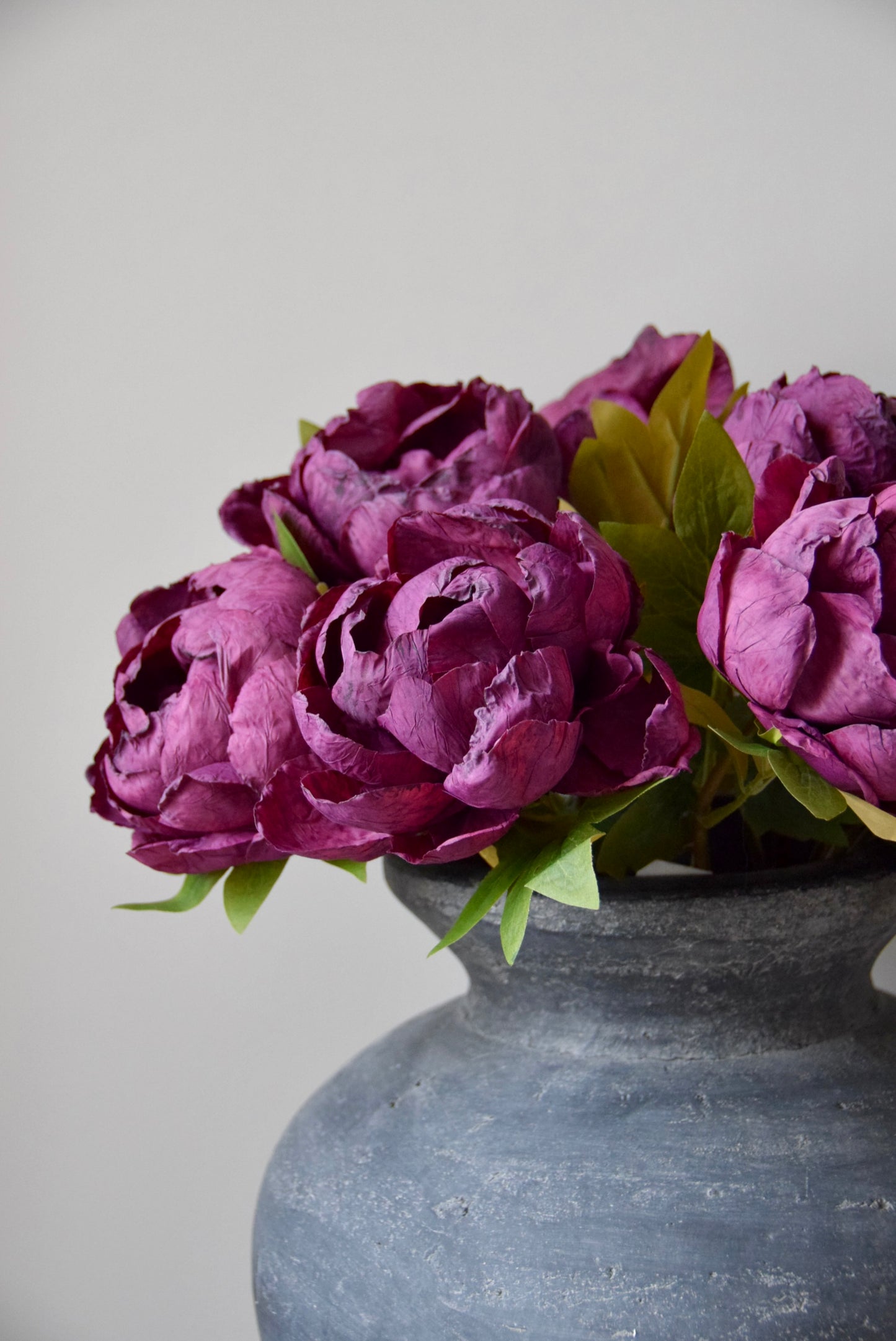 Burgundy flowers in a grey vase against a light grey background