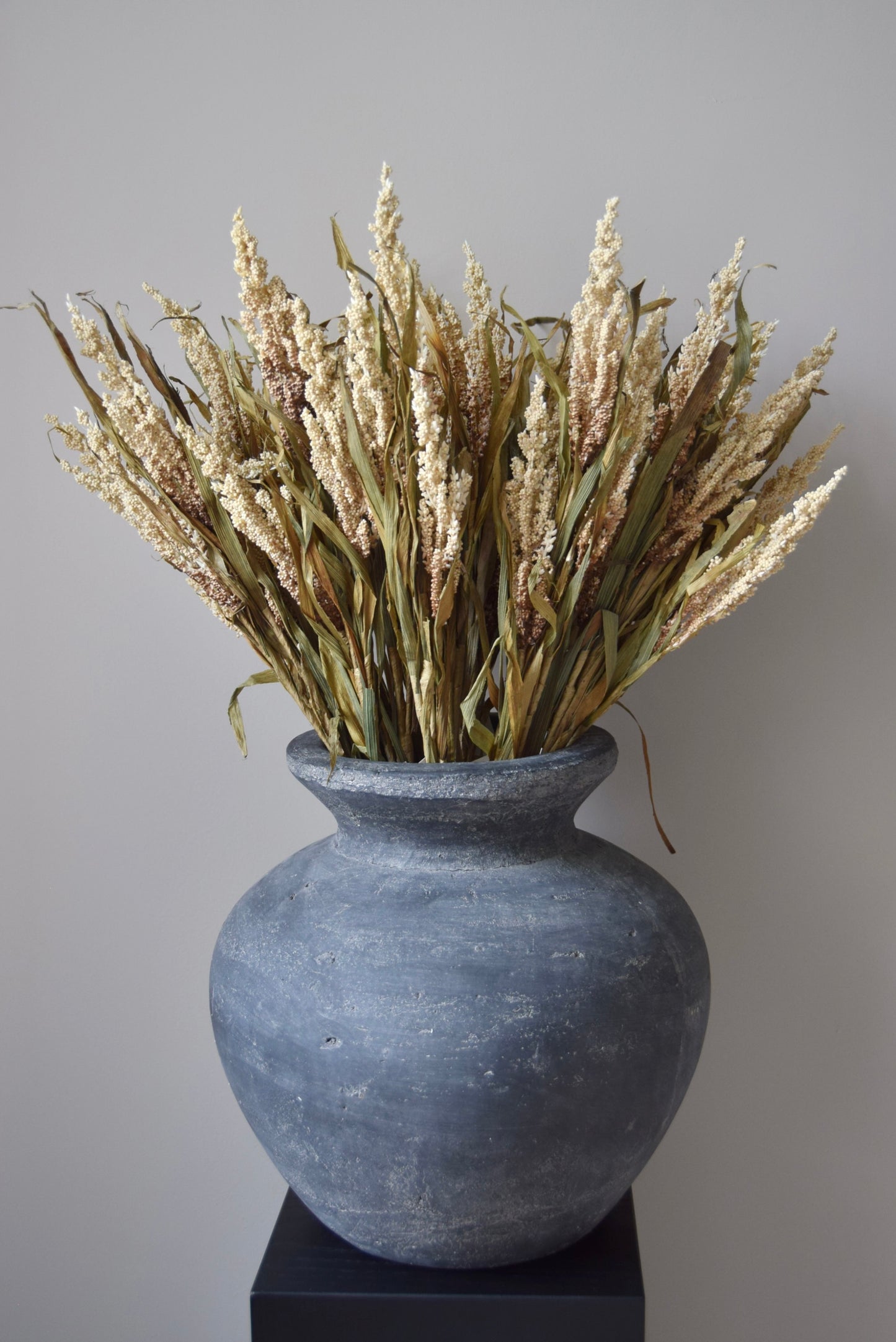Grey vase with dried plants against a plain background