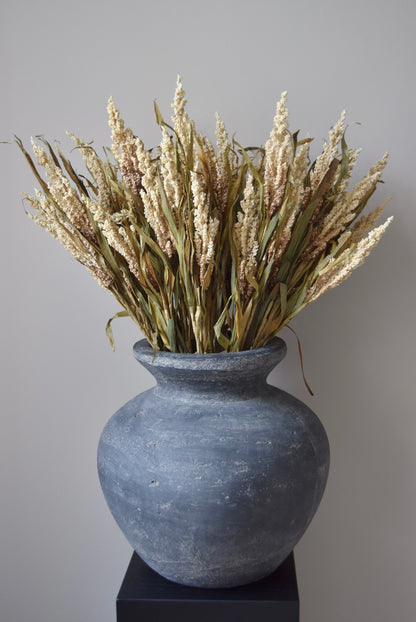 Grey vase with dried plants against a plain background