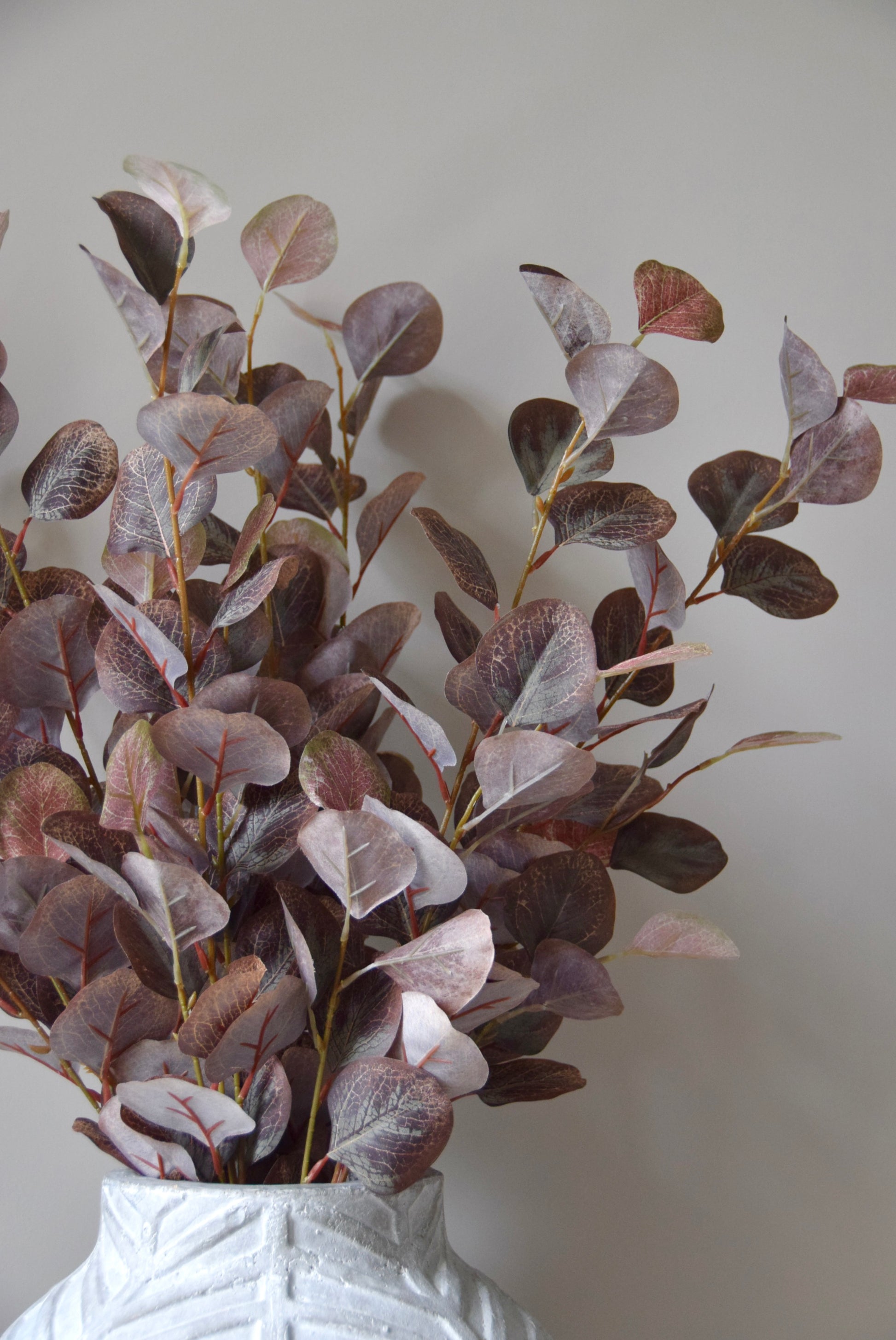 Artificial eucalyptus branches in a white vase against a plain background