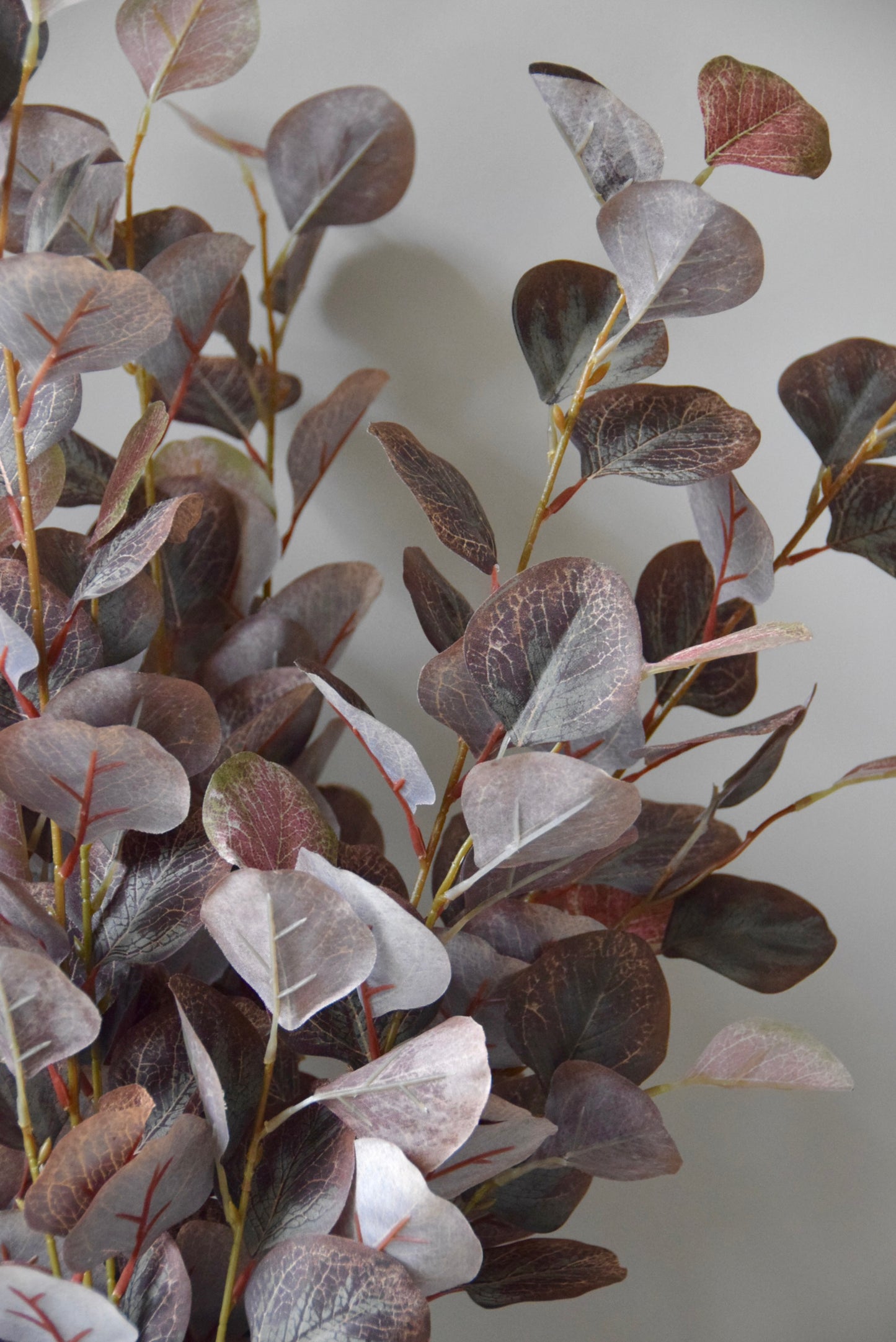 Artificial eucalyptus branches with purple and green leaves on a plain background