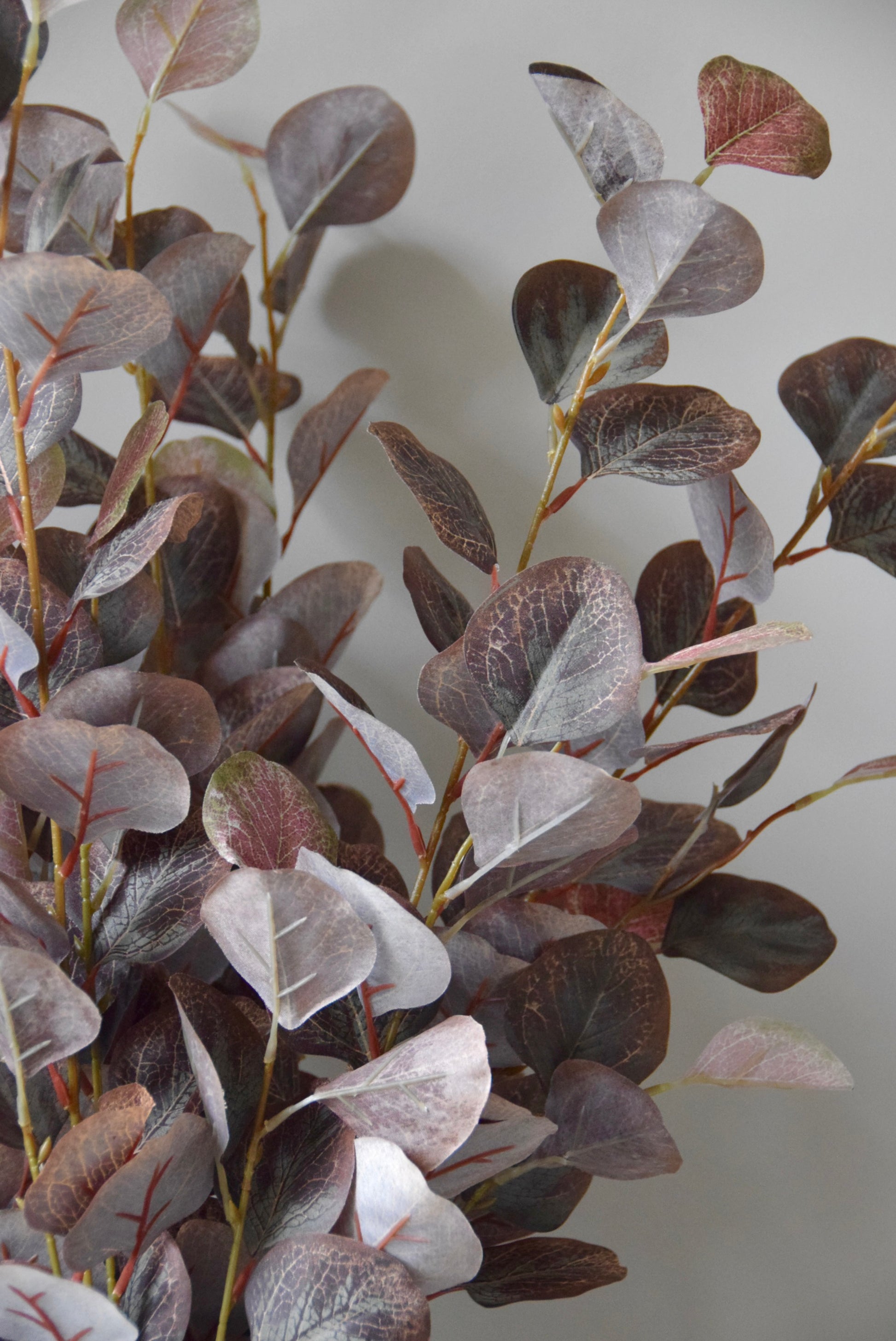 Artificial eucalyptus branches with purple and green leaves on a plain background