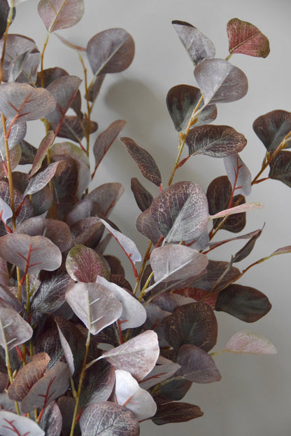 Artificial eucalyptus branches with purple and green leaves on a plain background