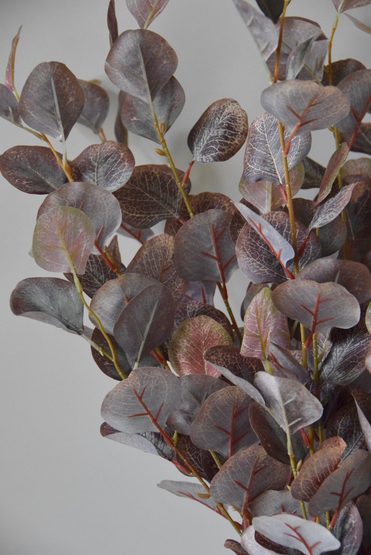 Artificial eucalyptus branch with purple and green leaves on a light grey background