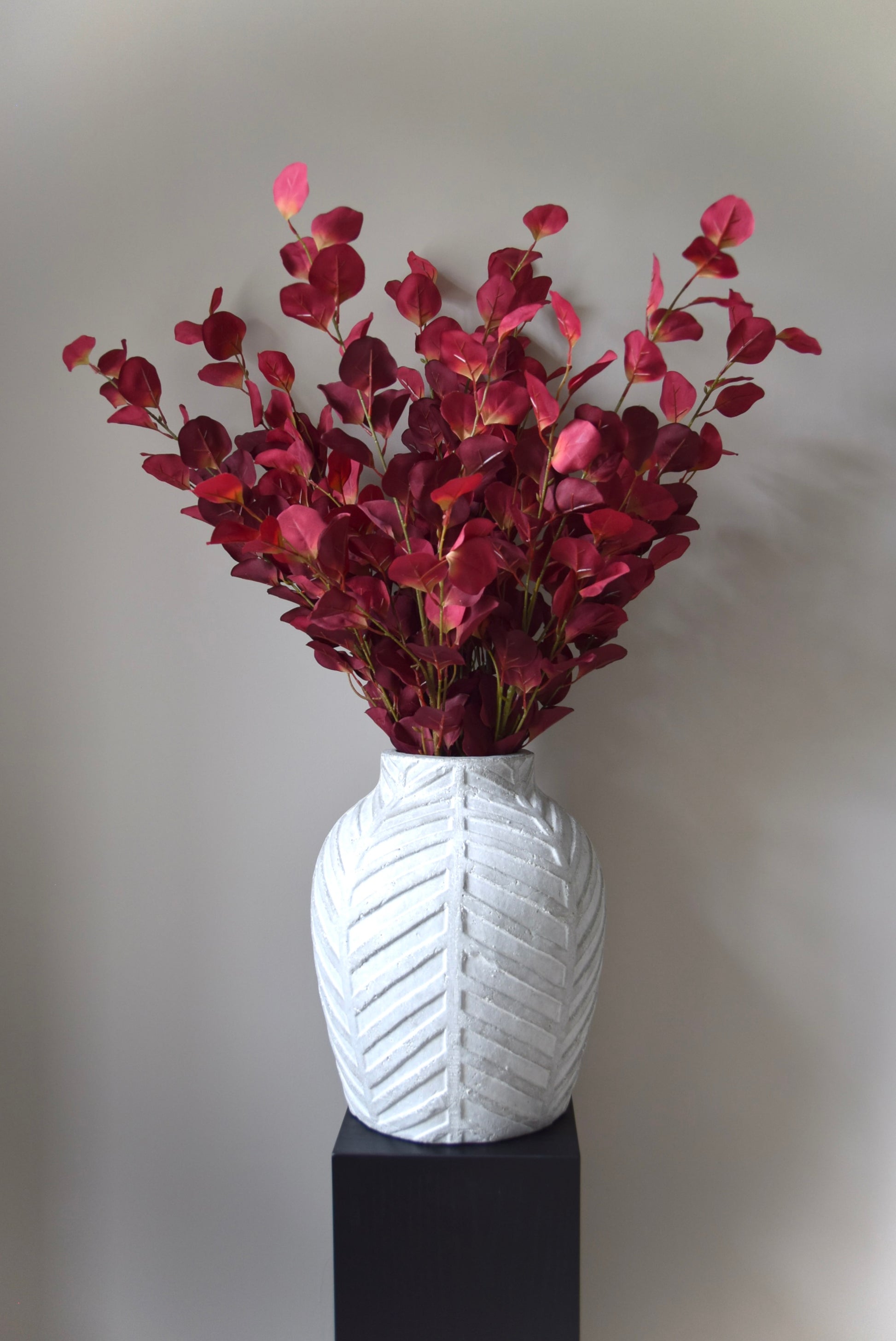 White textured vase with red leaves on a grey background