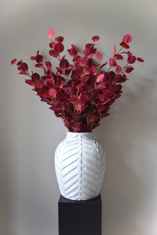 White textured vase with red leaves on a grey background