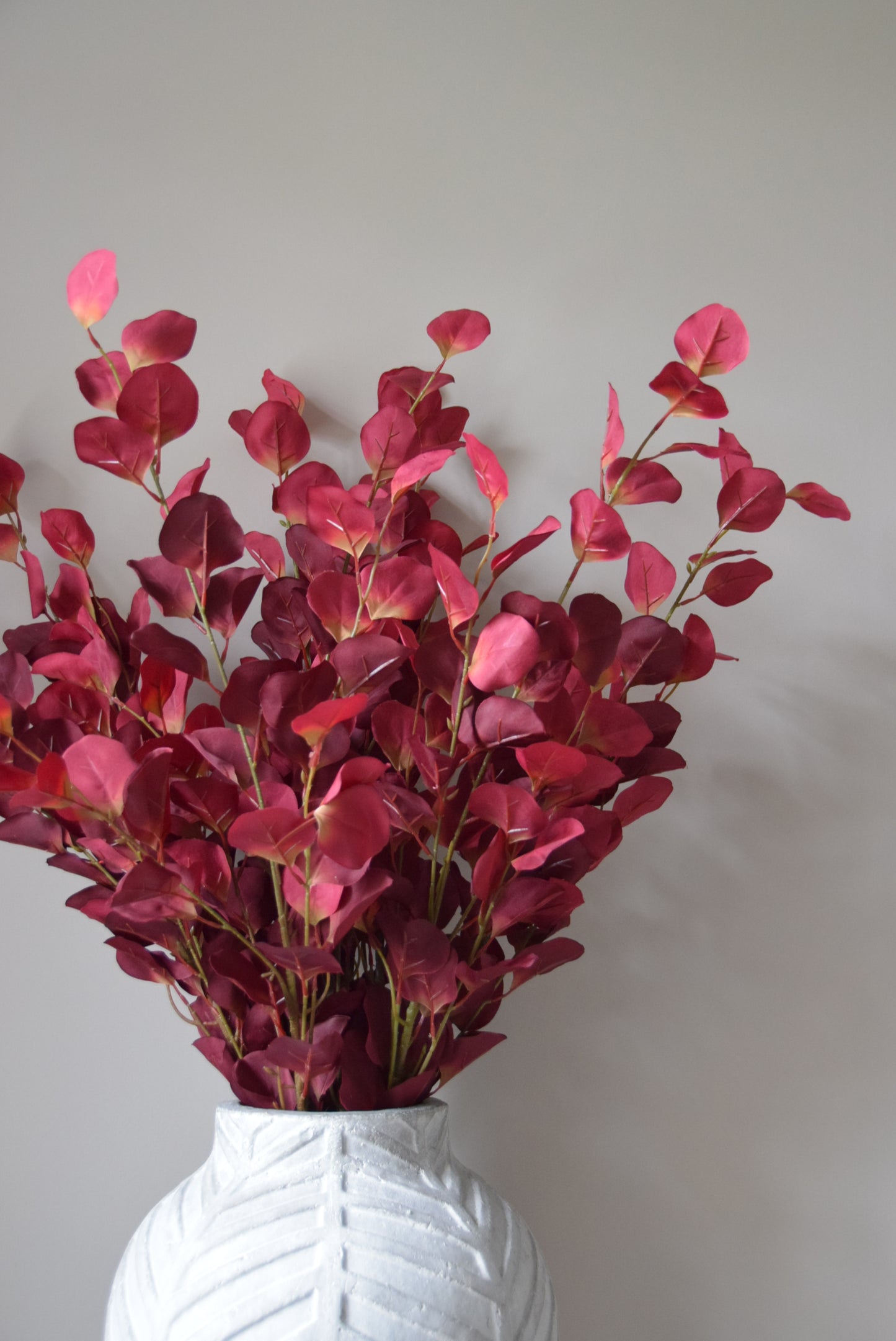 Bouquet of red eucalyptus in a clear vase against a plain background