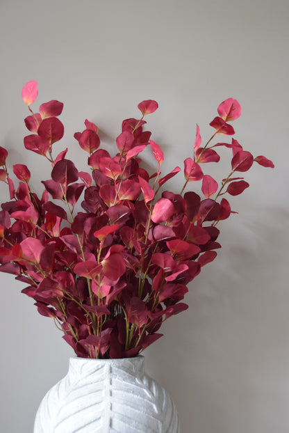 Bouquet of red eucalyptus in a clear vase against a plain background