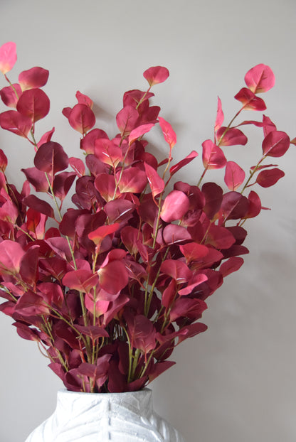 Bouquet of red artificial eucalyptus against a plain background