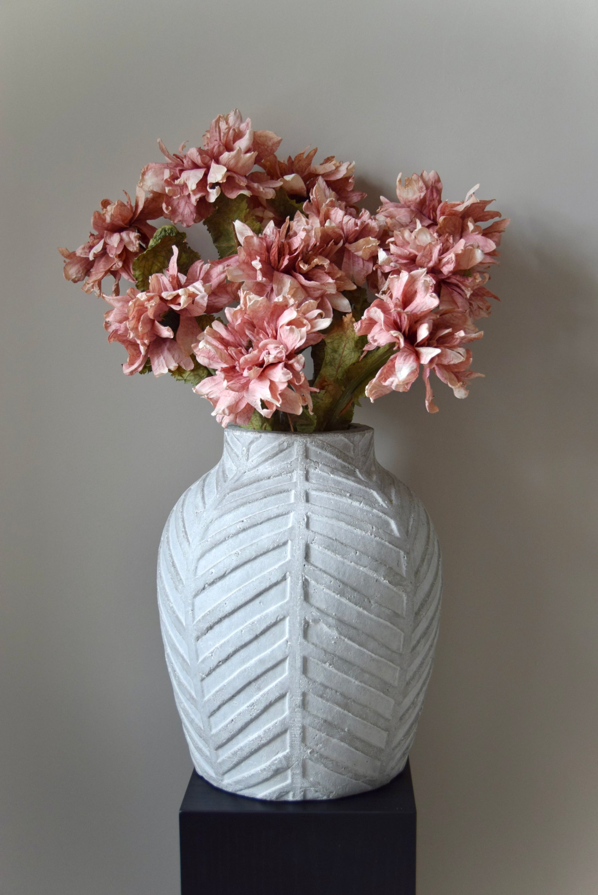 White textured vase with pink flowers against a plain background