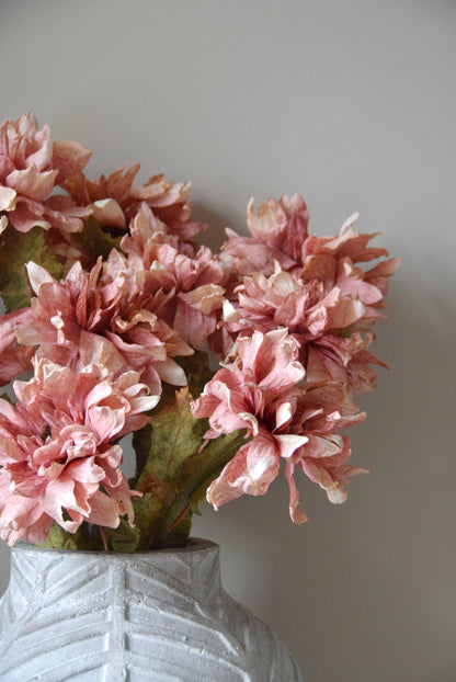 Pink flowers in a textured white vase against a plain background
