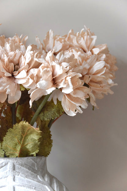 Close-up of beige flowers in a textured white vase against a light background