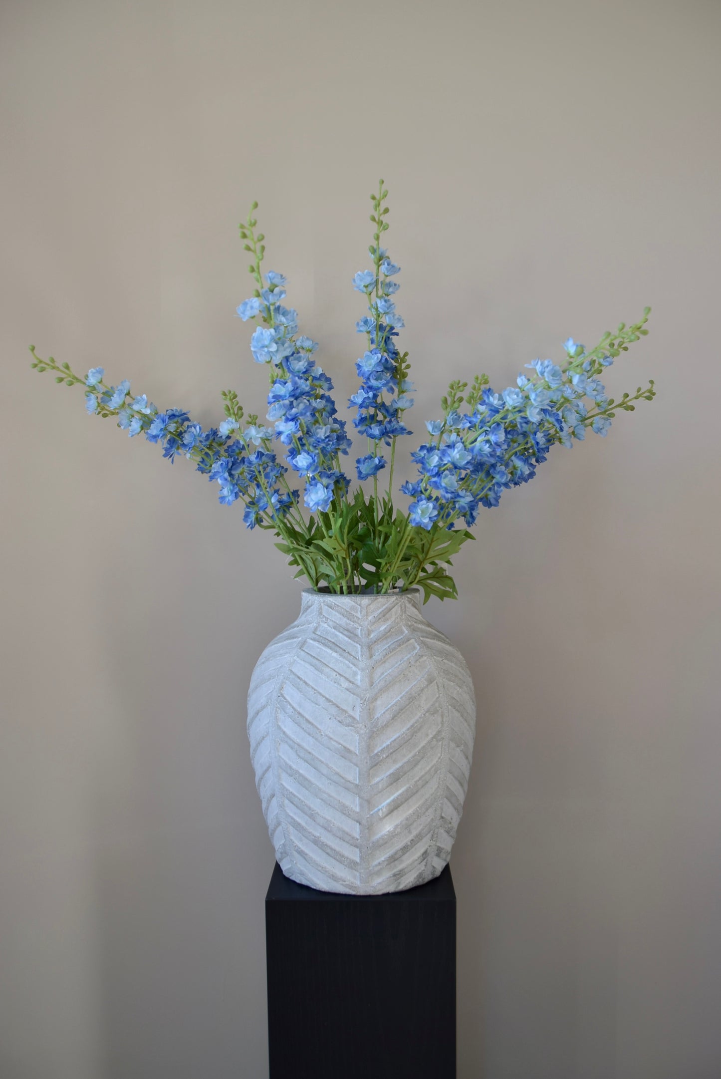 A bunch of artificial blue delphinium stems displayed in a stone chevron style vase.