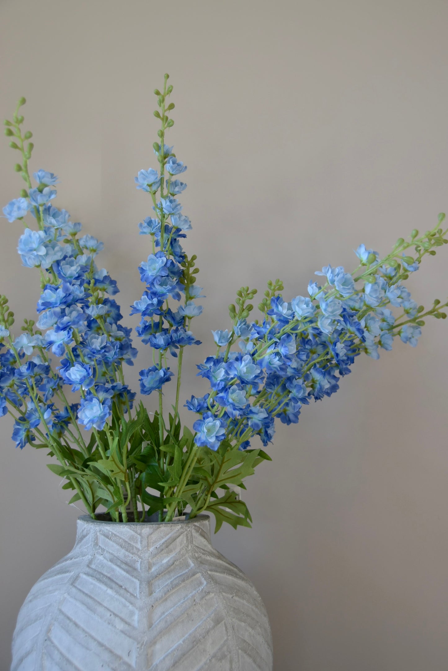 A bunch of artificial blue delphinium stems displayed in a stone chevron style vase.