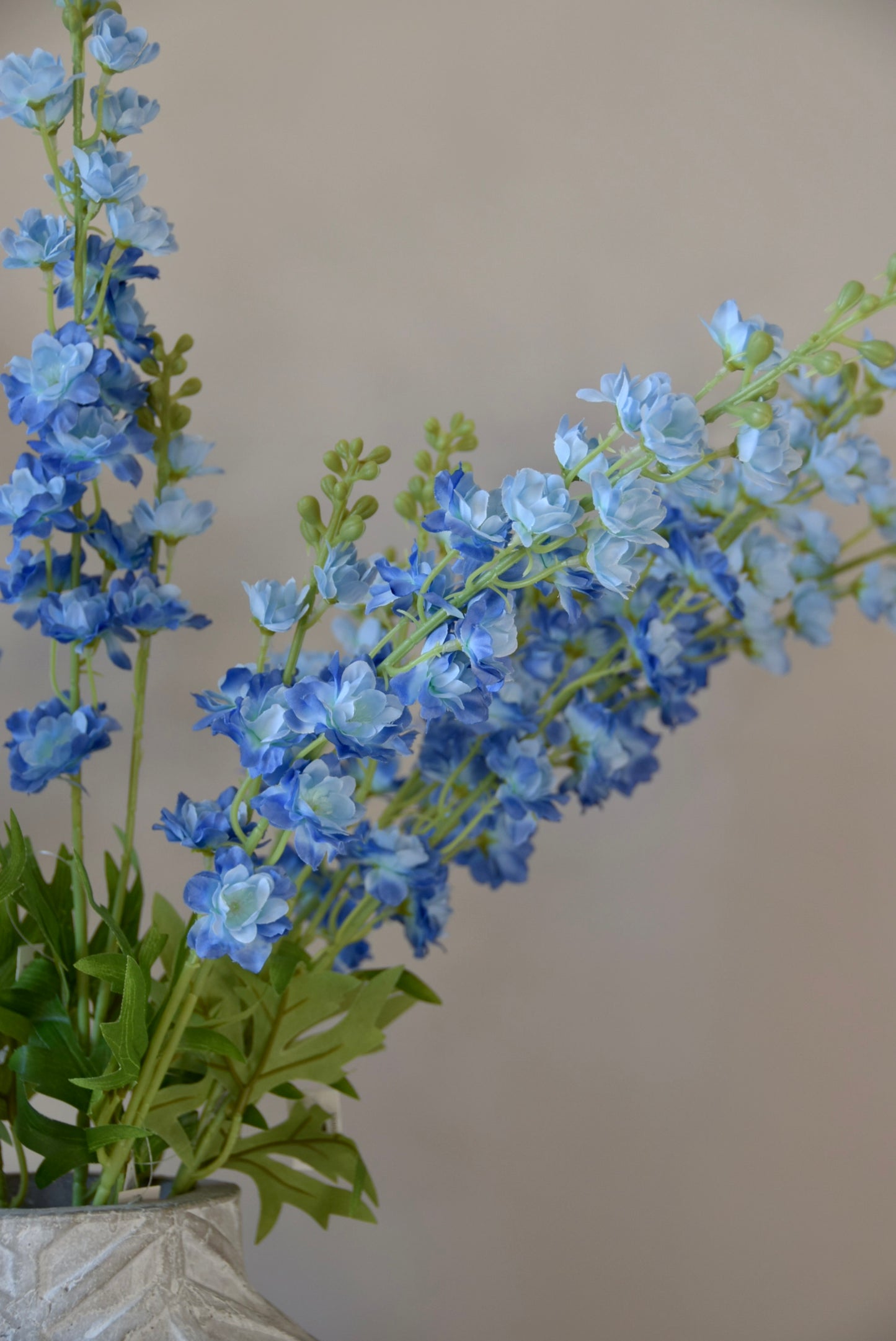 A close up of artificial blue delphinium stems in a vase.