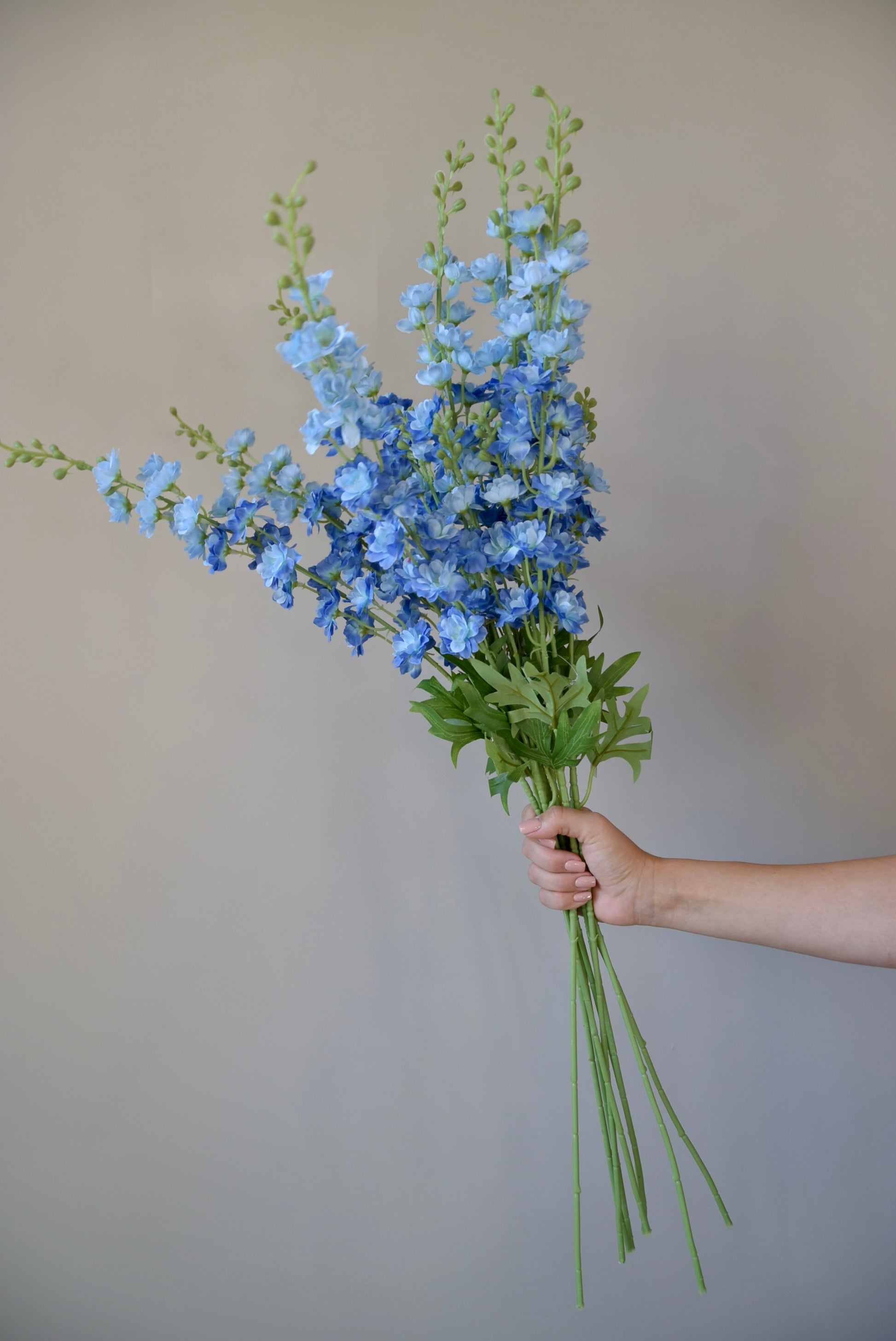 A hand holding a bunch of artificial blue delphinium stems.