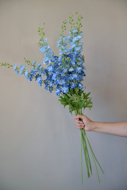 A hand holding a bunch of artificial blue delphinium stems.
