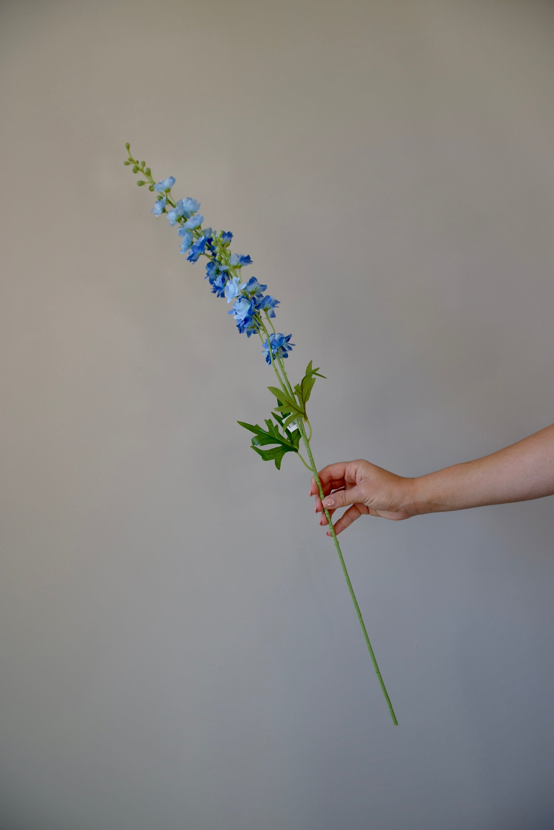 A hand holding a single artificial blue delphinium stem.