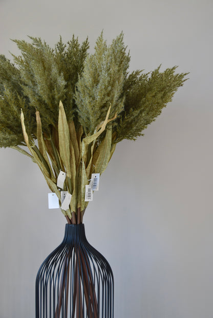 Bouquet of dried green plants in a black wire vase against a plain background