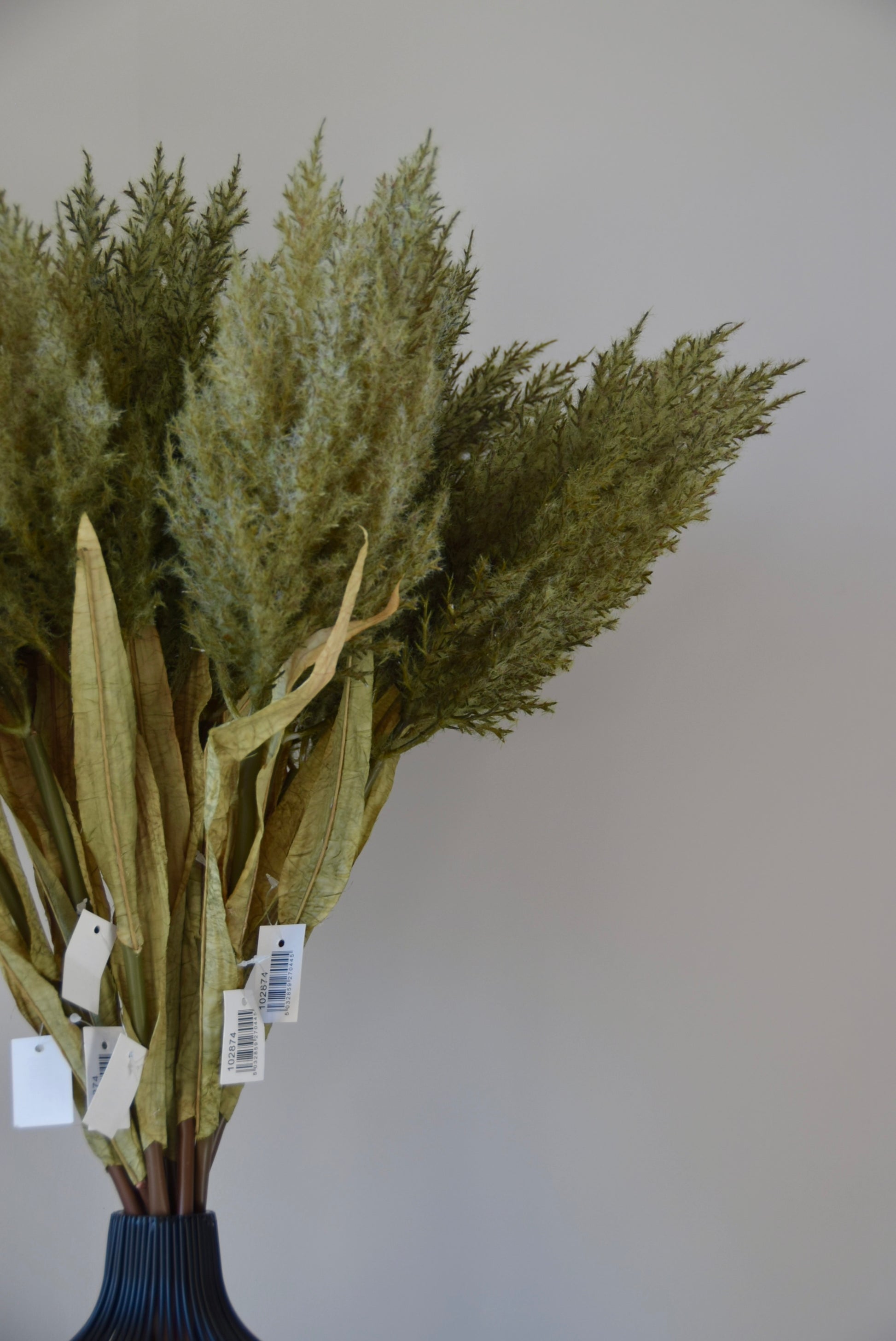 Bouquet of artificial greenery in a dark vase against a plain background