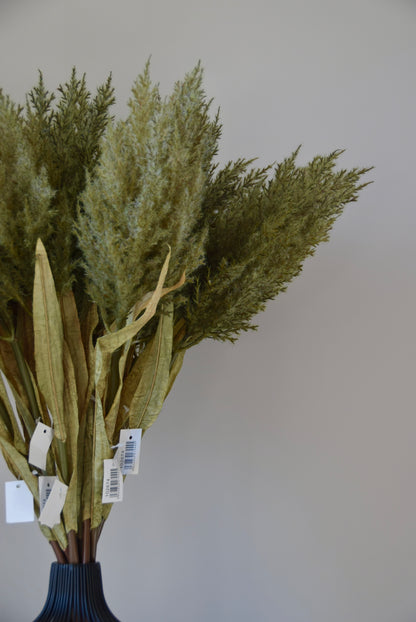 Bouquet of artificial greenery in a dark vase against a plain background
