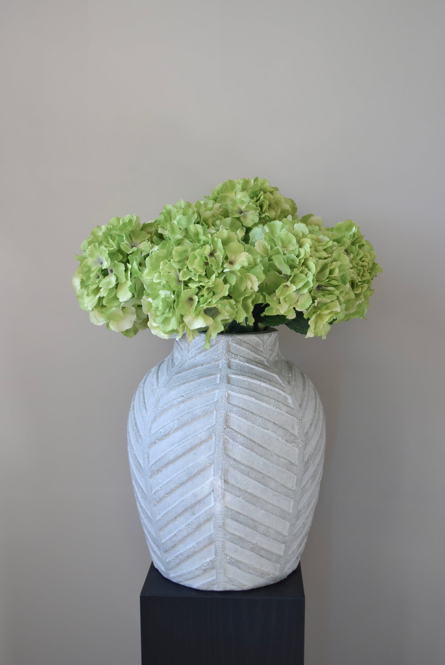White textured vase with light green flowers against a plain background