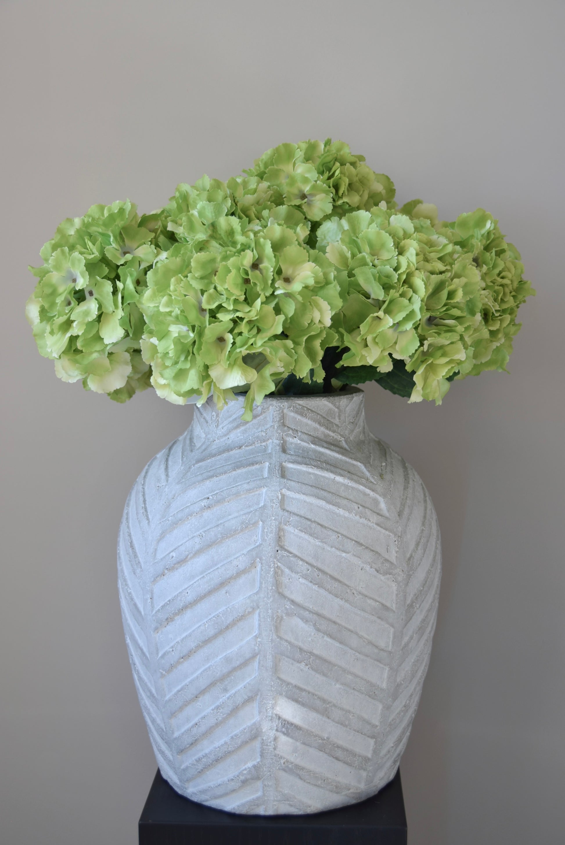 White textured vase with green flowers against a grey background