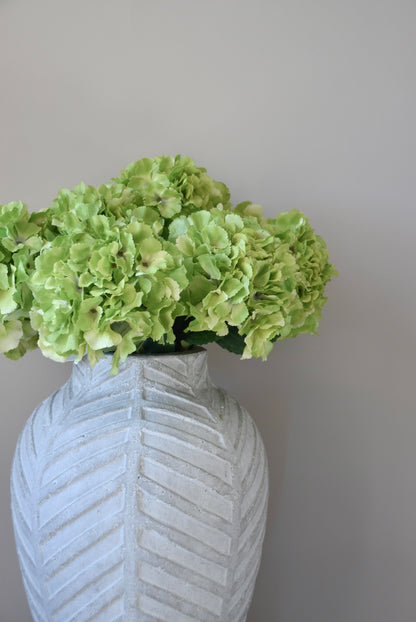 Stone textured vase with green flowers against a grey background