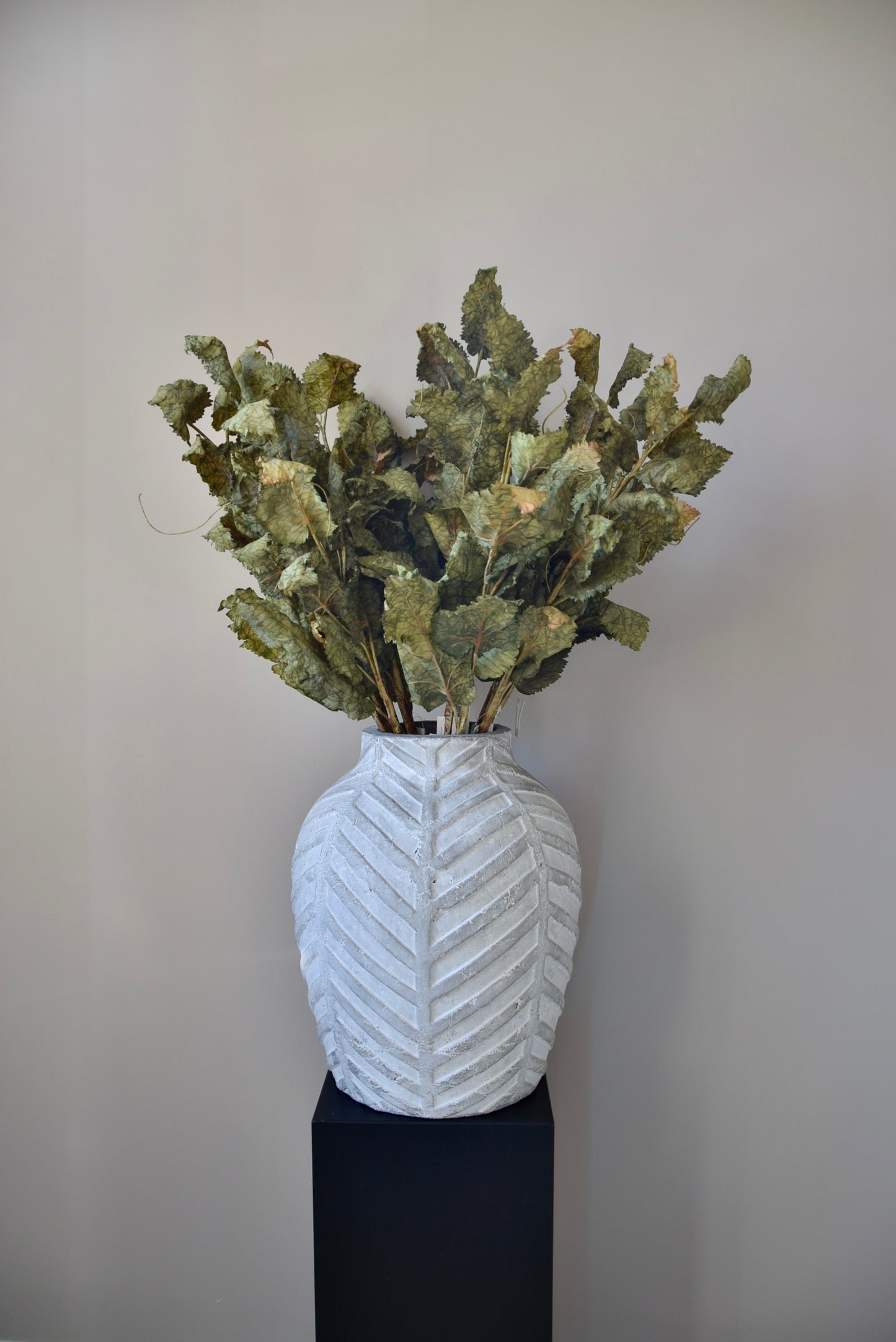 White textured vase with greenery against a plain background