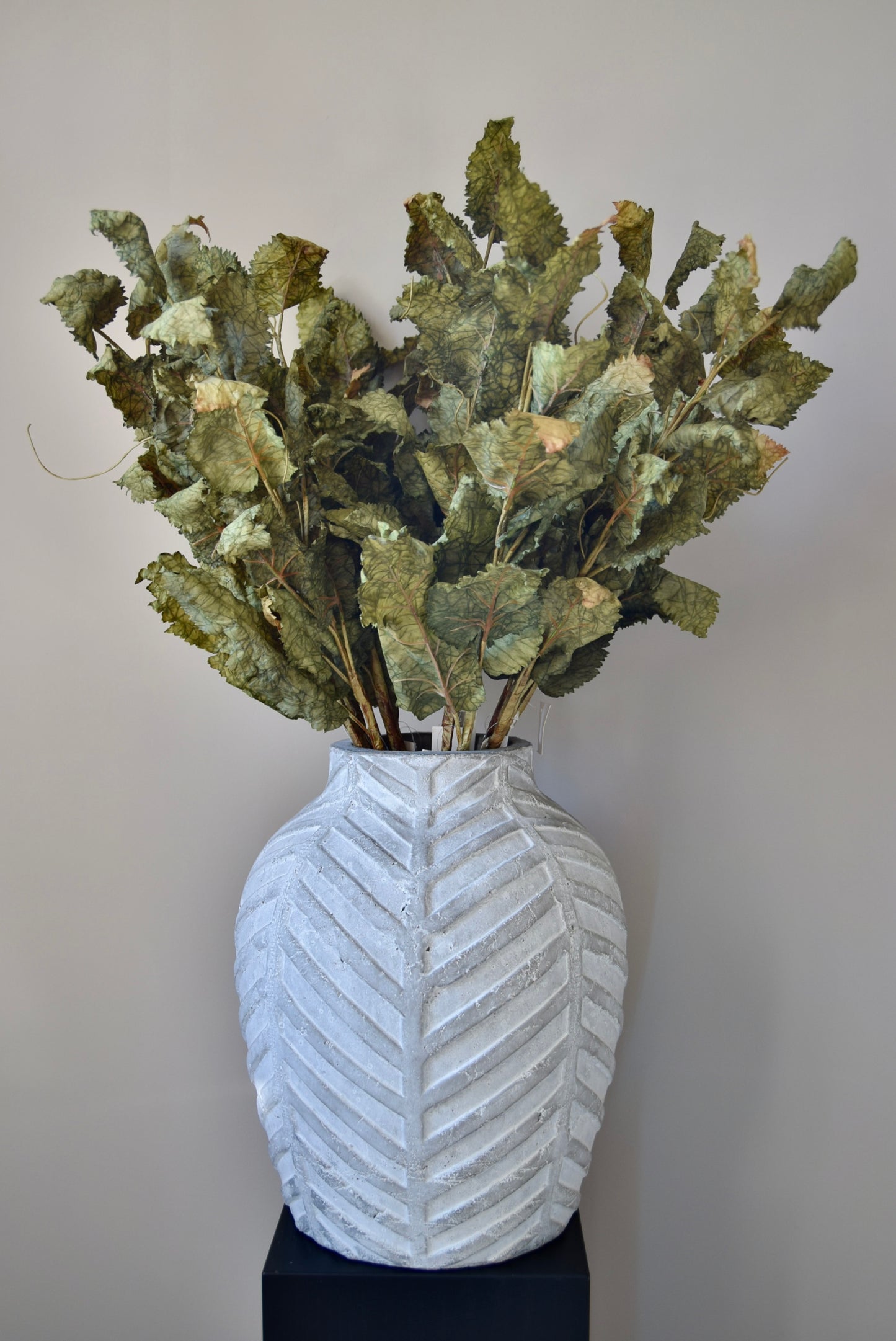 White textured vase with greenery against a plain background