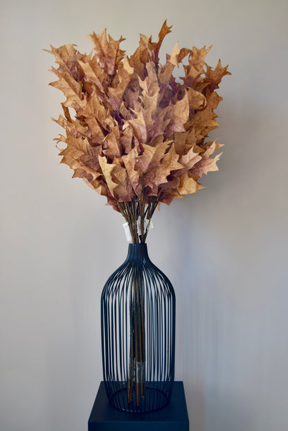 Decorative arrangement of dried leaves in a black cage-like vase on a plain background