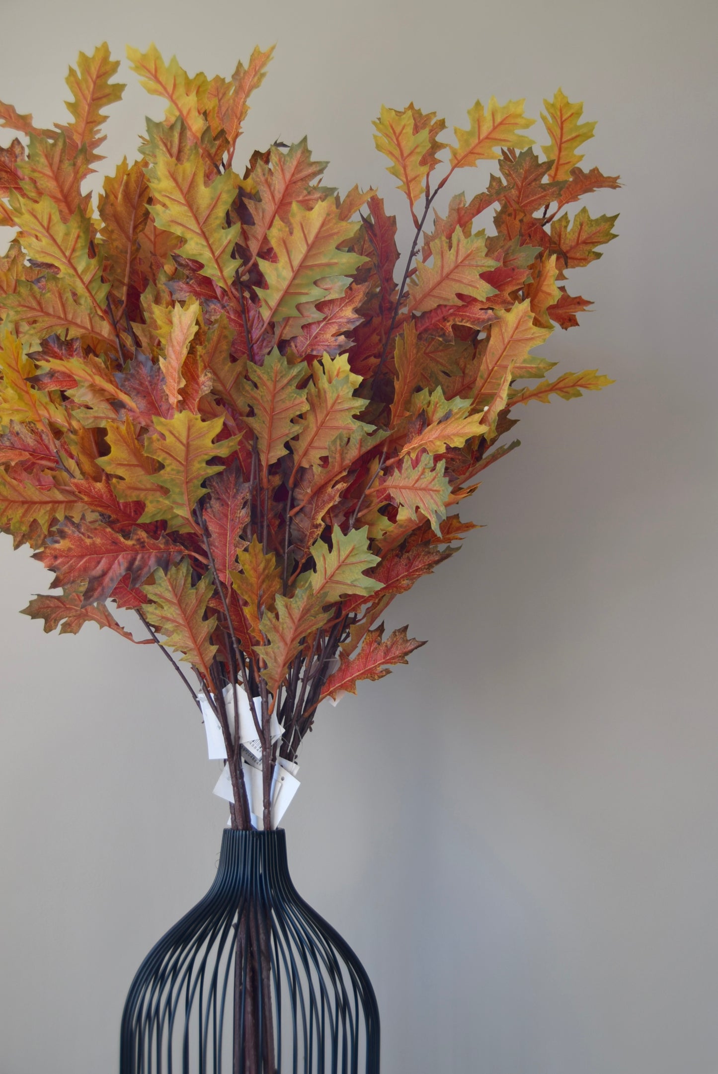 Bouquet of autumn leaves in a black vase against a plain background