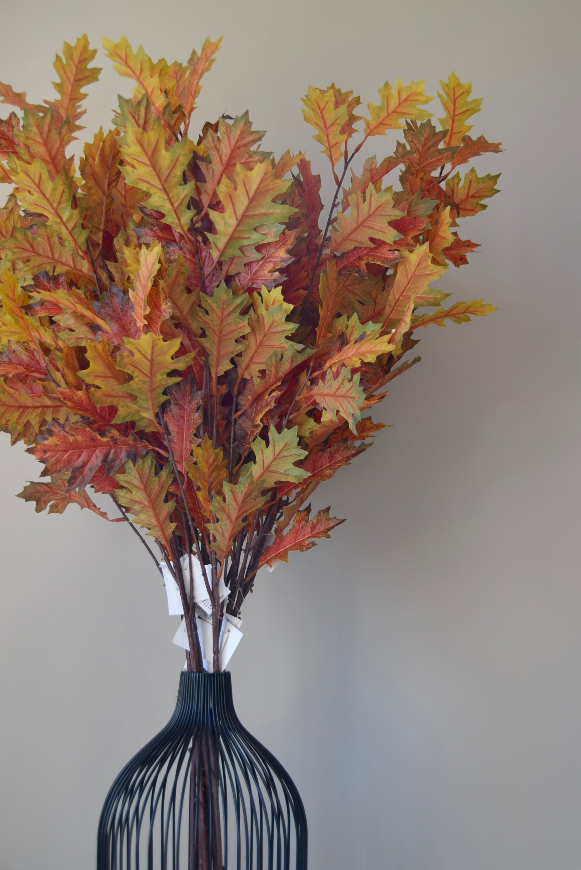 Bouquet of autumn leaves in a black vase against a plain background