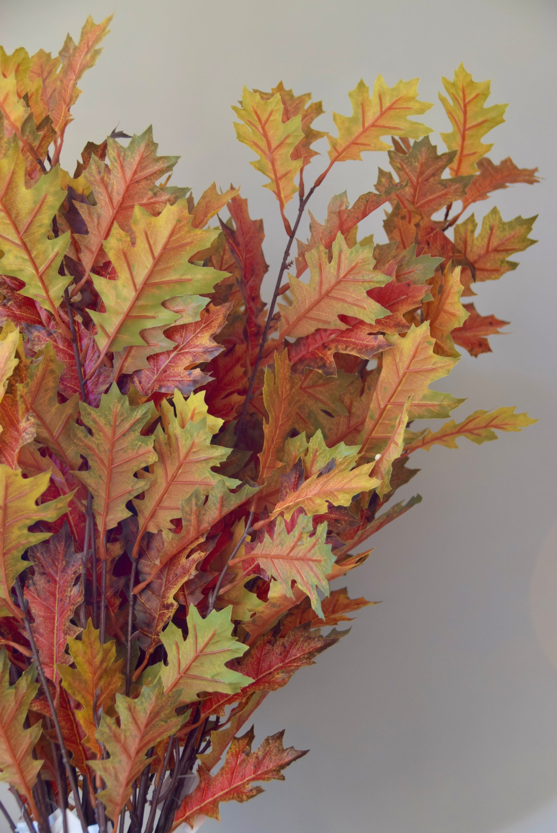 Artificial autumn leaf arrangement with red, orange, and green leaves on a plain background