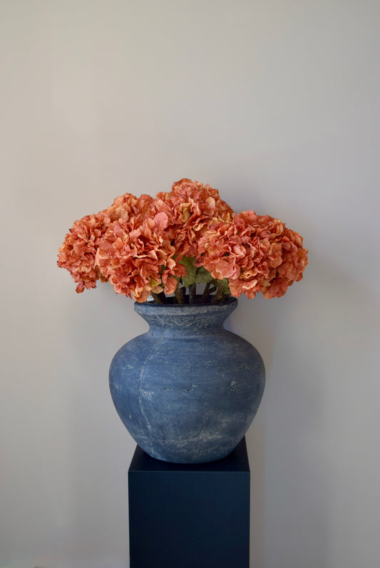 Grey vase with orange hydrangeas on a plain background