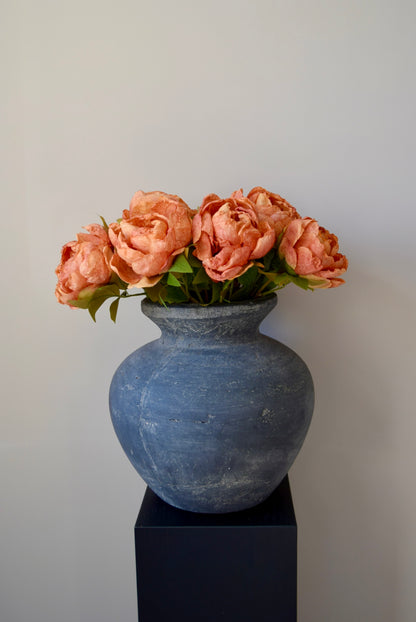 Grey textured vase with orange peonies on a black stand against a plain background