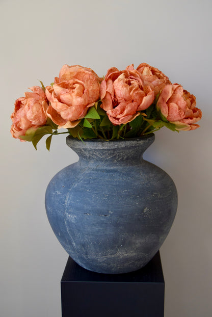 Grey textured vase with orange peonies on a black stand against a plain background