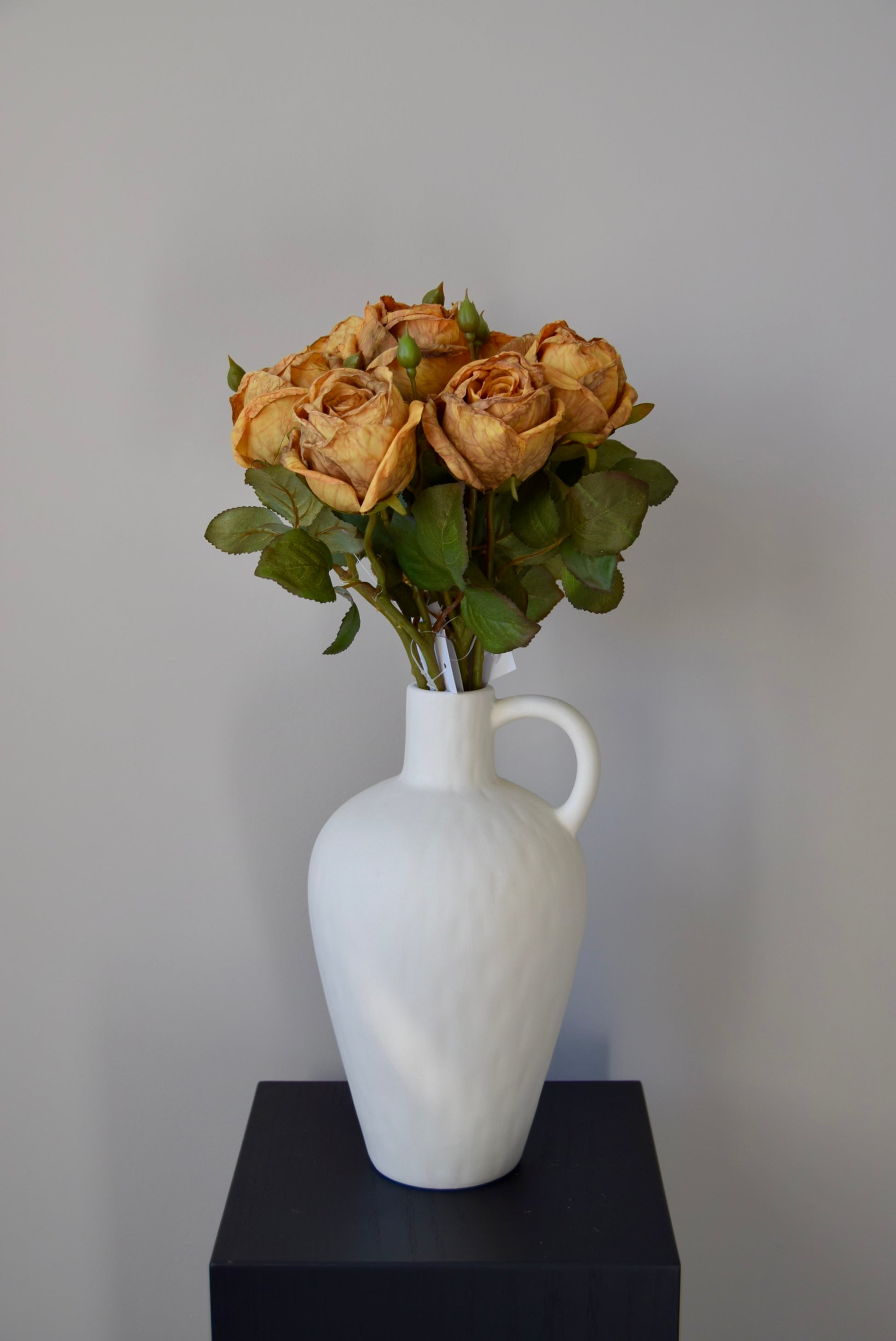 White vase with dried roses on a black surface against a grey background