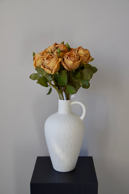 White vase with dried roses on a black surface against a grey background
